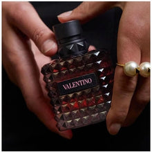Valentino perfume bottle with studded design held by a person wearing a pearl ring.